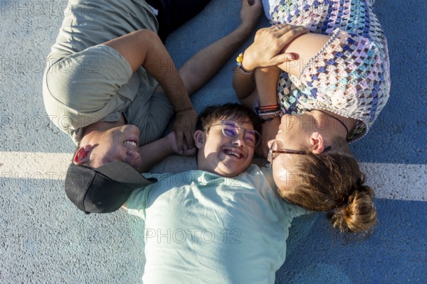 A teenager with Down Syndrome lying outdoors with family, enjoying a loving and joyful moment together Their smiles and relaxed demeanor showcase a strong family bond
