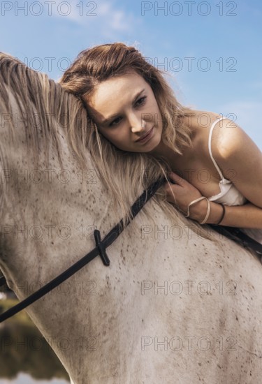 A serene scene of a young woman gently resting her head against a horse, conveying a deep connection and trust. The clear blue sky adds to the calm and peaceful atmosphere