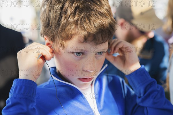Close-up of a young boy in a blue jacket, adjusting earphones, deeply focused, sitting in a tourist bus, with passengers in the background