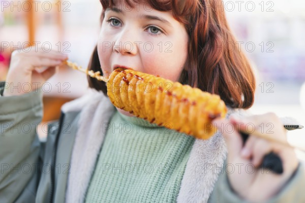A young girl enjoys a spiral tornado potato on a stick outdoors. The crispy, golden snack is seasoned and perfect for a casual street food experience