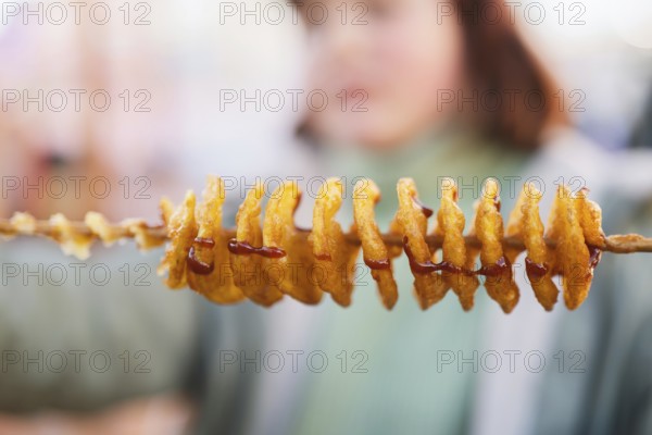 Close-up of golden-brown spiral tornado potatoes on a skewer, drizzled with savory sauce. This popular street food snack is crispy and visually appealing