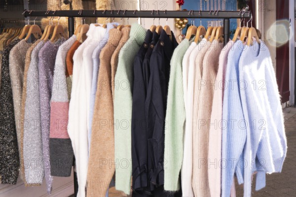 A collection of cozy wool and knit sweaters in various colors and textures hangs neatly on wooden hangers in a clothing store, showcasing stylish winter fashion trends
