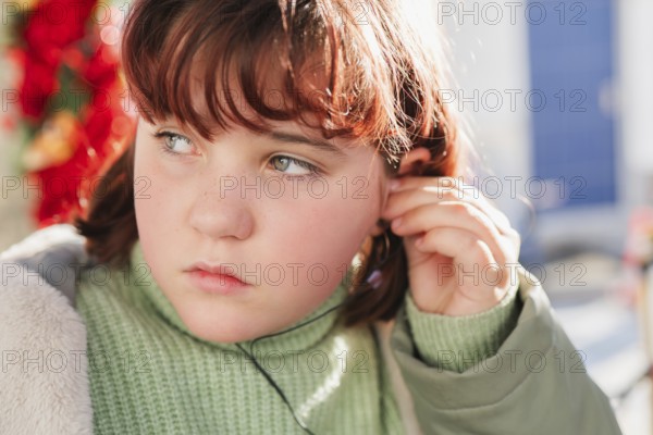 Close-up of a young girl adjusting her headphones, highlighting a thoughtful expression with a soft sunlight background
