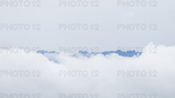 Ethereal view of jagged mountain peaks peering through a blanket of white clouds in San Ramon, Peruvian Amazon