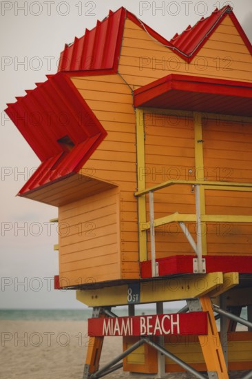 A vibrant, colorful lifeguard stand at Miami Beach, featuring a bold red and yellow color scheme against a subtle beach background