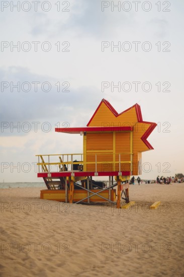 A bright red and yellow lifeguard tower stands vibrantly against a soft dusk sky on Miami Beach, showcasing the iconic coastal architecture