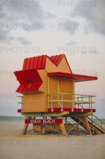 A colorful lifeguard stand at Miami Beach, featuring a bright red roof and yellow walls, representative of the vibrant architectural style unique to the area, captured at dusk under a moody sky