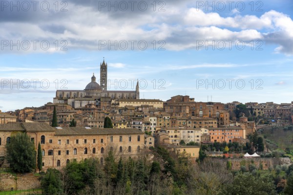A scenic view of Siena, Italy, featuring its historic architecture, the iconic Siena Cathedral, and a vibrant mix of stone buildings nestled amidst lush greenery under a cloudy sky