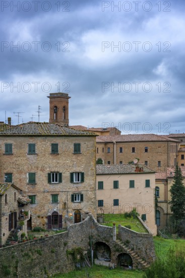 A charming view of Volterra, Tuscany, featuring traditional stone houses and rustic architecture. The medieval village is set against a dramatic cloudy sky, showcasing Italy's rich history