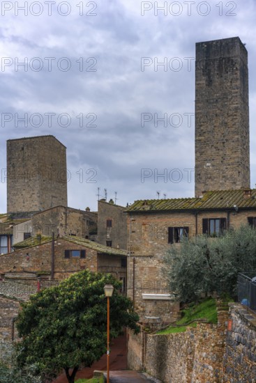 A panoramic view of San Gimignano, highlighting its famous medieval towers and traditional stone buildings. The lush greenery and cloudy sky add to the timeless beauty of Tuscany