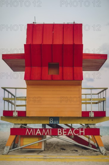 Vibrant red and orange lifeguard stand prominently positioned on Miami Beach, captured during a cloudy day, showcasing the unique architecture and eye-catching colors against a serene beach background