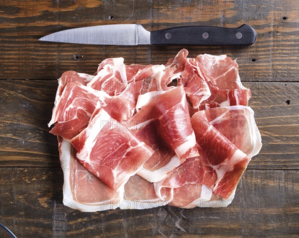 Thinly sliced cured ham arranged on a wooden board beside a sharp kitchen knife, highlighting the texture and rich color of the meat