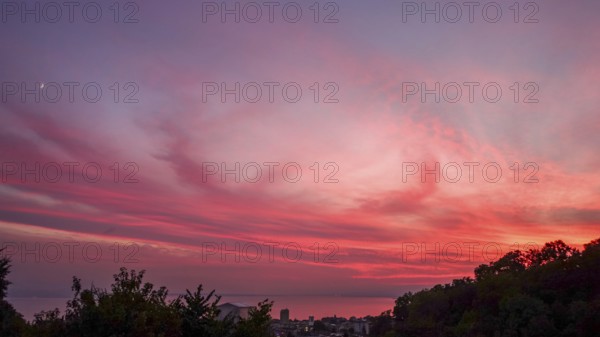 Captivating view of a vivid sunset painting the skies in shades of pink and red, over Lausanne and Lake Leman, highlighting the serene landscape and tranquil waters