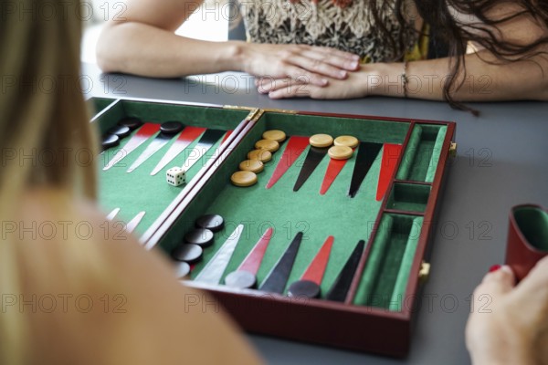 Close-up of a backgammon board with pieces and dice in play Mother and daughter are engaged in a strategic, casual game, showing anticipation and focus on the outcome