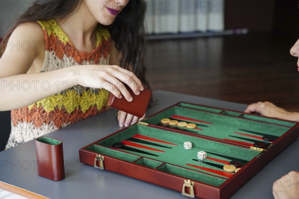 A woman engaging in a strategic game of backgammon, rolling the dice in anticipation A green and red board with game pieces highlights leisure time and strategy