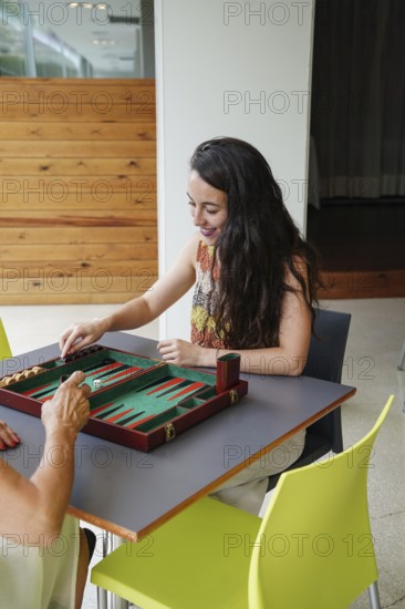 Mother and daughter are playing backgammon inside a cozy room The board is set on a table, and they are focused on the game, surrounded by a modern and comfortable setting