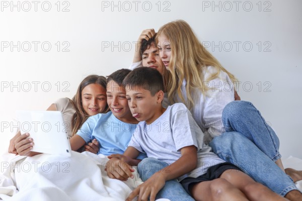 A heartwarming family portrait featuring an older brother and sister enjoying a fun moment with their younger triplet siblings, consisting of a girl and two boys, as they interact with a digital tablet
