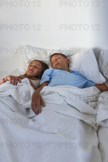 A young girl and boy, are captured sleeping peacefully side by side in a bright, cozy bed setting, exemplifying serene childhood moments