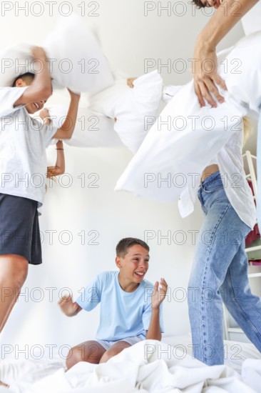Family with five members, including a young girl and two boys who are triplets, along with their older siblings, enjoy a playful pillow fight in a bright bedroom setting