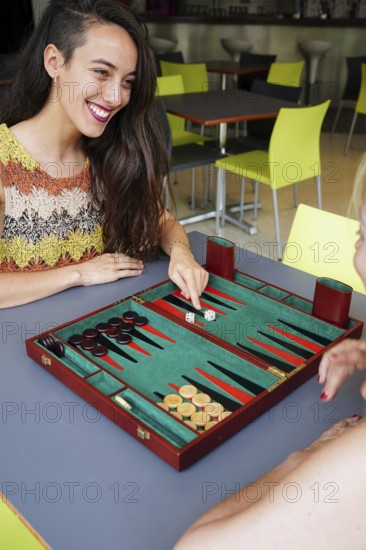 Mother and daughter engaged in a friendly game of backgammon at a cafe, The vibrant setting adds warmth and joy to the gaming experience
