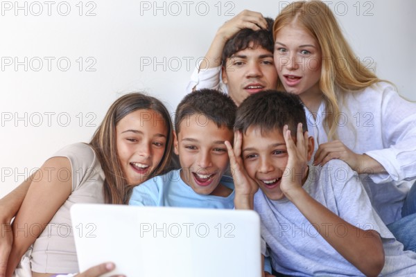 Five siblings, including a girl and two boy triplets, enjoy time with their elder brother and sister, all engaging with a laptop at home