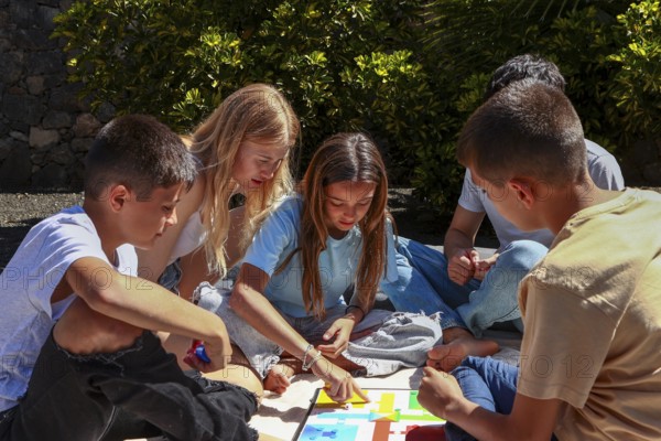 A heartwarming scene as five siblings, including triplet boys, a girl, and their older brother and sister, gather outdoors to play a colorful board game