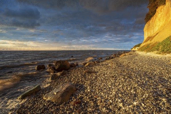 Chalk cliffs and rocky beach with boulders on the Baltic Sea in morning light under dark sky with dramatic clouds, Jasmund National Park, Rügen Island, Mecklenburg-Western Pomerania, Germany