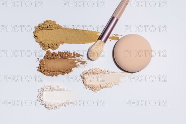 Top view of colorful, assorted face powders and a cosmetic brush on a light surface, showcasing shades from light to dark and highlighting both compact and loose types