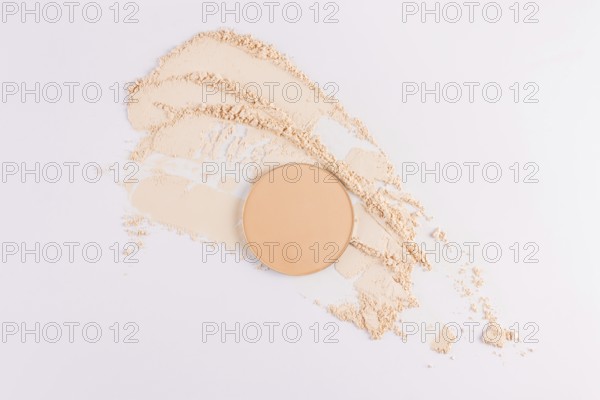 Top view of a circular compact powder alongside scattered loose face powder on a clean, white background. Ideal for depicting cosmetics and beauty products