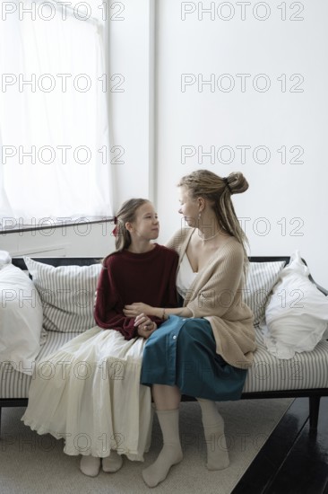 A heartwarming image of a woman and a young girl sitting on a sofa in a cozy living room, sharing a joyful moment with smiles Sunlight filters through a nearby window