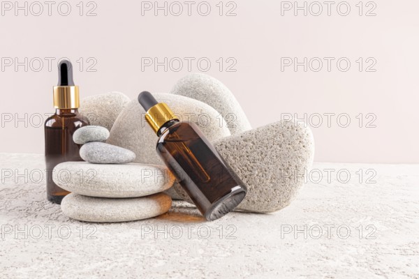 Two amber glass serum bottles with golden caps are artfully displayed among smooth gray stones, evoking a serene and spa-like ambiance for relaxation and skincare