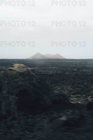 Serene Lanzarote landscape featuring vast volcanic plains and distant, hazy mountains under a muted sky, capturing the barren beauty and mystique of the island