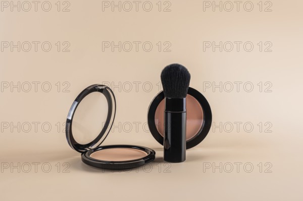 Open compact powder alongside a professional makeup brush, creatively arranged against a soft beige backdrop. The minimalist design emphasizes the elegance of the beauty products