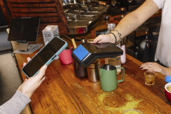 A customer uses a smartphone for contactless payment at a trendy specialty coffee shop, showcasing modern technology amid coffee preparations like mugs and espresso