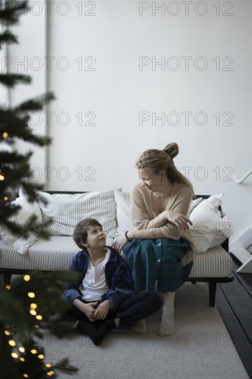 A warm holiday moment, a mother and child share smiles in a cozy living room with festive decor A lit Christmas tree adds charm to the peaceful, joyful atmosphere