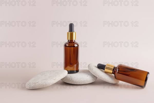 Two amber dropper bottles are artistically arranged on stacked smooth stones against a subtle beige background, creating a balanced and minimalist aesthetic