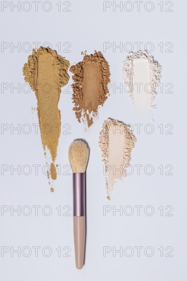 Top view of three different shades of face powder scattered artistically next to a makeup brush on a light blue background