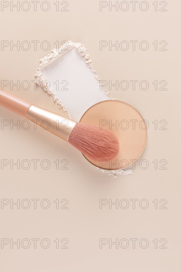 Top view of a makeup brush and compact powder next to loose powder on a beige surface, ideal for beauty and cosmetic themes