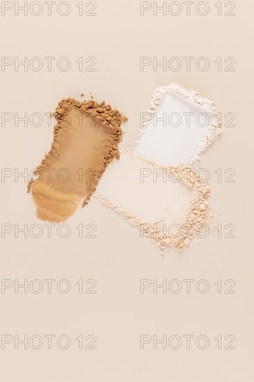 Top view of a split representation of compact and loose face powders, spilled on a beige background. The image precisely captures the texture and contrasting forms of the makeup