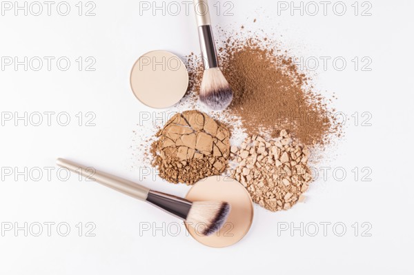 Top view image showcasing a selection of makeup powders including compact and loose varieties, along with professional brushes. A crushed compact next to a loose powder heap illustrates different textures and uses in makeup application