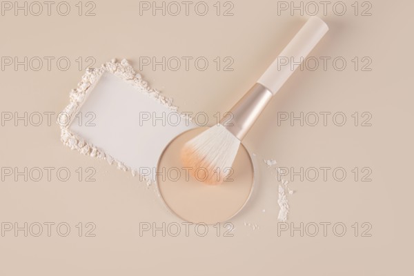 Top view of a makeup setting displaying a compact with loose face powder beside it, scattered gently around a soft brush on a pastel background