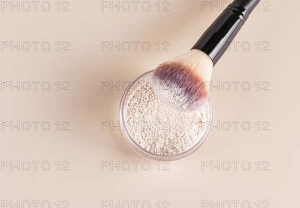 Top view of a makeup brush with pink and white bristles partially dipped into loose face powder, showcased on a smooth beige background, illustrating essential beauty products with a focus on texture and application