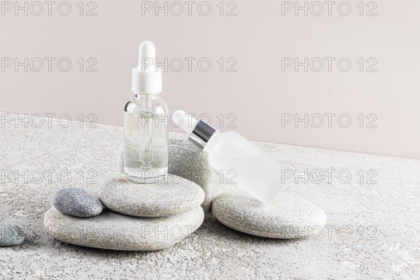 Two glass dropper bottles with clear and frosted finishes are placed elegantly on a stack of natural stones The minimalistic backdrop enhances their serene presentation