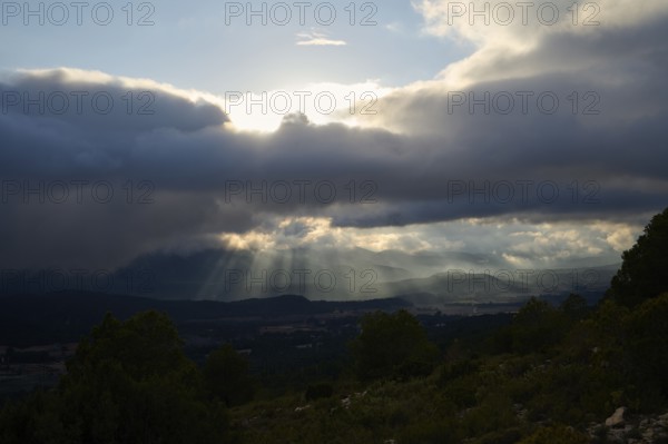 A breathtaking view of sunlight piercing through thick clouds over rolling hills and valleys, creating a dramatic and serene landscape in Alicante, Spain