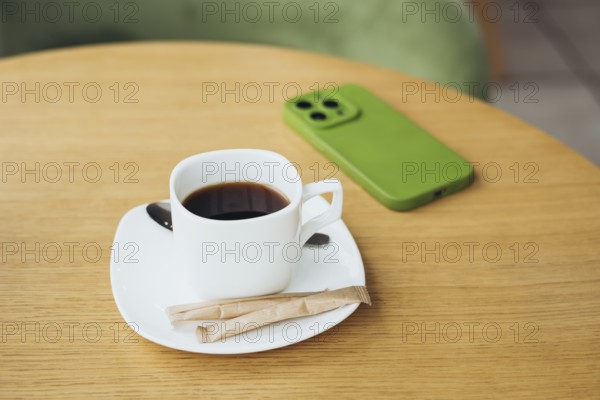 A cozy scene featuring a cup of coffee on a wooden table with a smartphone in a green case The simple, natural setting invites relaxation and focus