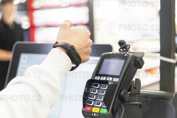 Cropped image of woman's hand making a payment using a smartwatch at a card terminal in a supermarket. The focus is on the interaction between the device and his watch