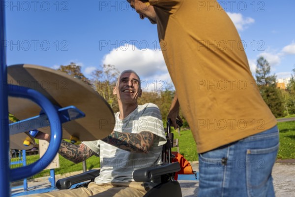 Friends enjoy a sunny day in the park, focusing on inclusive fitness for cerebral palsy One is using a wheelchair-accessible exercise machine, smiling, and interacting with a standing friend
