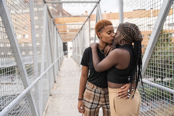 An LGBT multiethnic couple shares a tender embrace and kiss on a lively urban bridge. The vibrant setting captures their affection and highlights the beauty of diversity and love