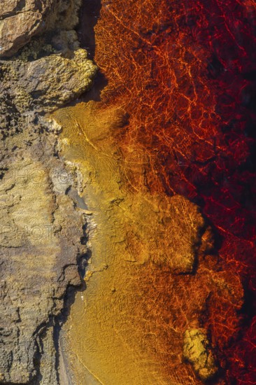 Striking aerial view of the Riotinto River, capturing its vibrant red and orange hues meeting rocky terrain Located in Huelva, Spain, this river is renowned for its unique mineral-rich waters