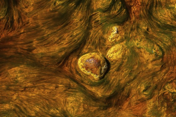 Close-up of the mineral-rich waters in Riotinto, Huelva, Spain, showcasing the vibrant orange and yellow hues swirling around stones in an abstract, textured pattern